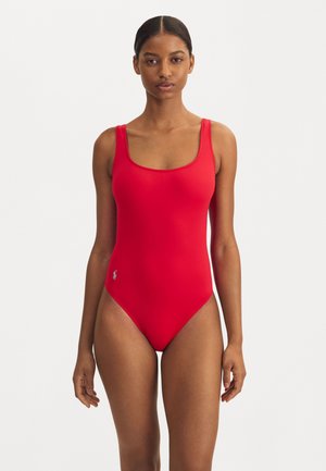 Bañador rojo de una sola pieza con escote redondo, tirantes anchos y pierna de corte alto. Tiene un pequeño logo en color contrastante cerca de la cadera.