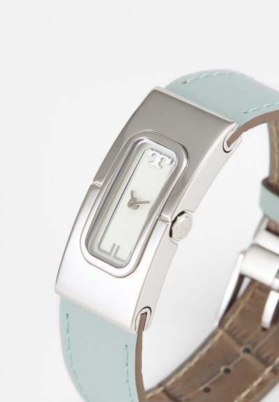 Orologio in metallo argento con cassa rettangolare, vetro trasparente, cinturino in pelle verde chiaro e retro in pelle marrone. Quadrante bianco minimalista con accenti argentati.