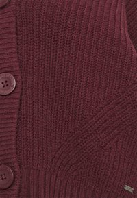 Bordowy sweter kardigan z dzianiny, z teksturowanym wzorem ściśle, z okrągłymi guzikami i małym metalowym logo na dolnej części.