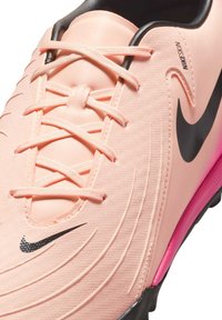 Világos rózsaszín focicipő fekete részletekkel, texturált felülettel, látható fűzőkkel és élénk rózsaszín sarokkal. A cipőn egy fekete Nike pipa logó található.