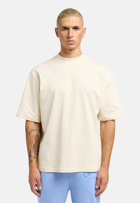 Light beige short-sleeve t-shirt made of soft cotton, featuring a subtle embossed logo on the chest and a relaxed fit.