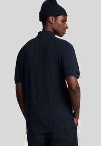 Marineblå polo-shirt med korte ærmer og klassisk krave, lavet af glat stof med en fitted silhuet og subtile design detaljer.