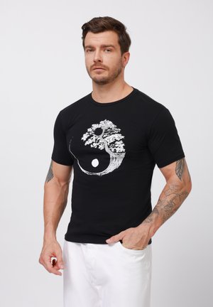 Black short-sleeve t-shirt featuring a white tree and circle graphic in a yin-yang style. Made of soft fabric with a classic crew neckline.