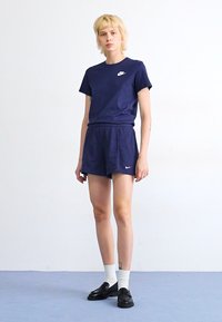 T-shirt à manches courtes Nike bleu marine et shorts assortis. Présente un petit logo blanc sur la poitrine. Le modèle porte des chaussettes blanches et des chaussures noires.