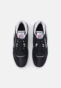 Zapatillas deportivas negras de material textil y ante, con acentos blancos, parte superior texturizada y cordones. Logo de Reebok en la lengua.