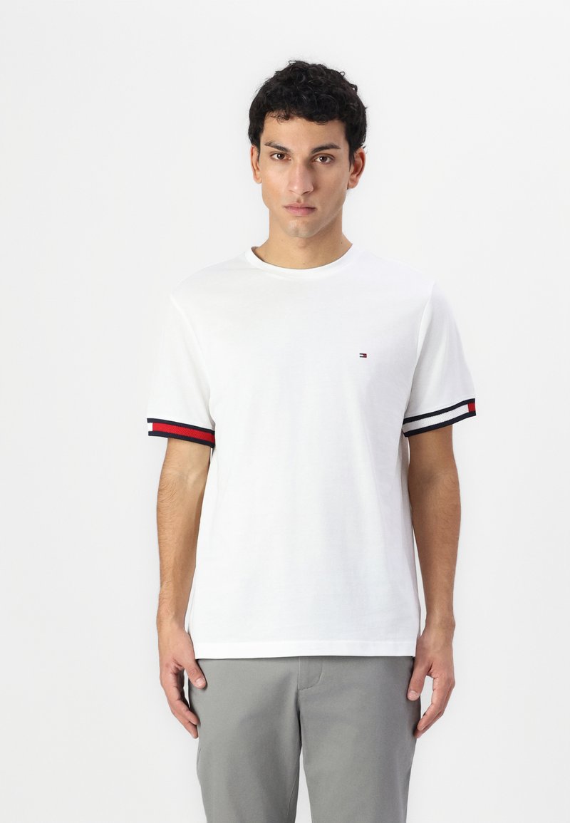 Hvid kortærmet t-shirt med rund hals, prydet med marineblå og røde striber på ærmerne og et lille logo på brystet.