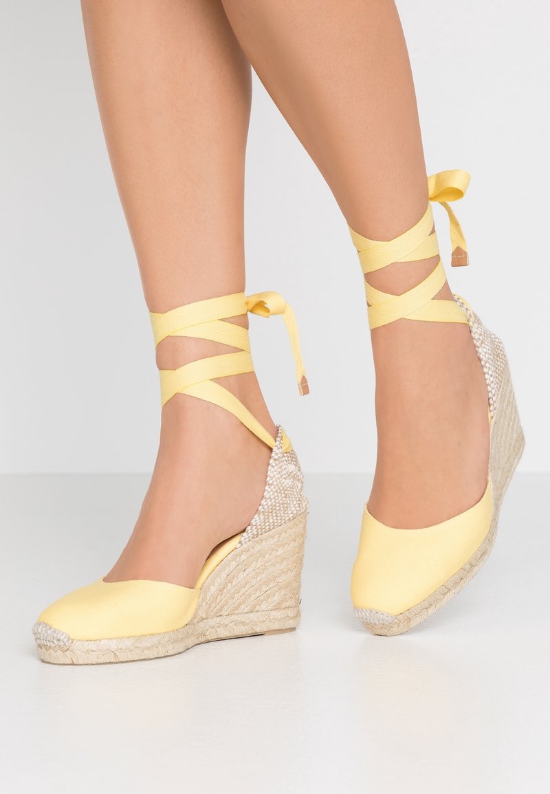Chaussures compensées jaunes en espadrille avec un talon en jute tissé et texturé, une tige en tissu et des brides à la cheville croisées en ruban.