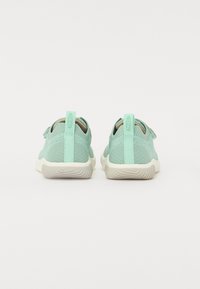 Zapatillas de color verde menta claro con una parte superior de tela texturizada, cierre con correa ajustable y una suela de crema flexible y estriada.