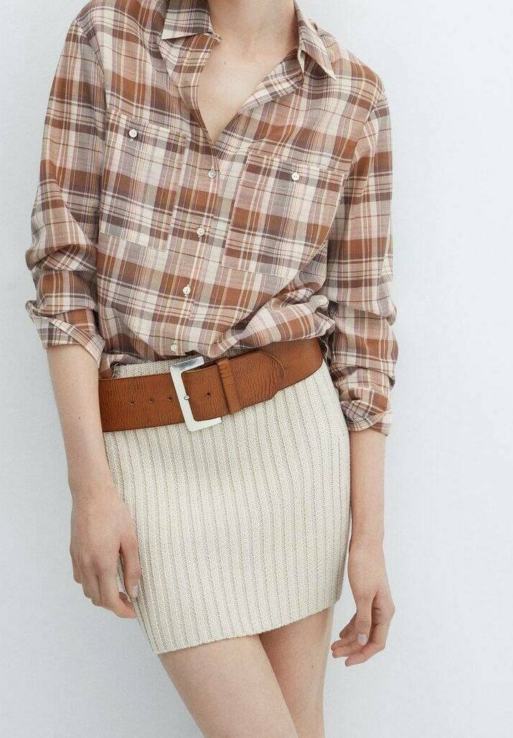 Donna che indossa una camicia a quadri marrone con bottoni, infilata in una mini gonna in maglia a coste beige, con una ampia cintura marrone.