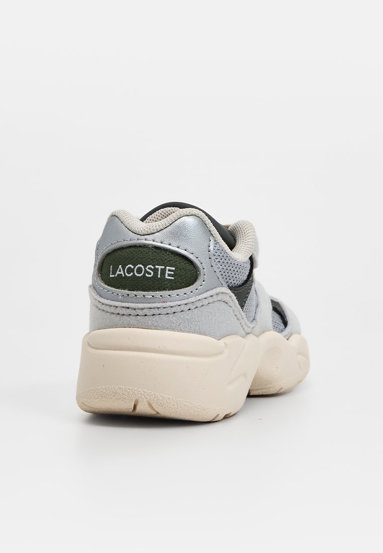 Szare i czarne sneakersy z teksturowaną siateczkową górą, gumową podeszwą i zielonym logo Lacoste na pięcie. Wyróżniają się wyściełanym kołnierzem dla większego komfortu.