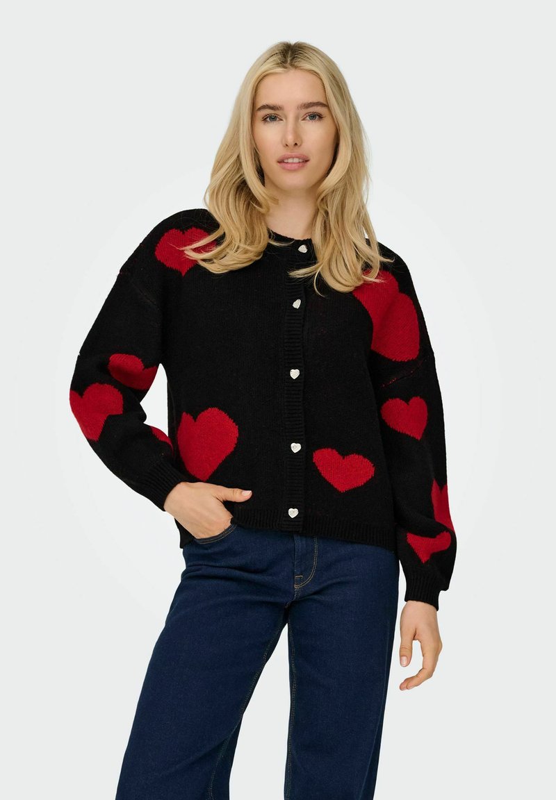 Svart cardigan med röda hjärtmönster, rund halsringning och silverfärgade hjärtformade knappar. Ribbad ärm- och fållkant ger textur.