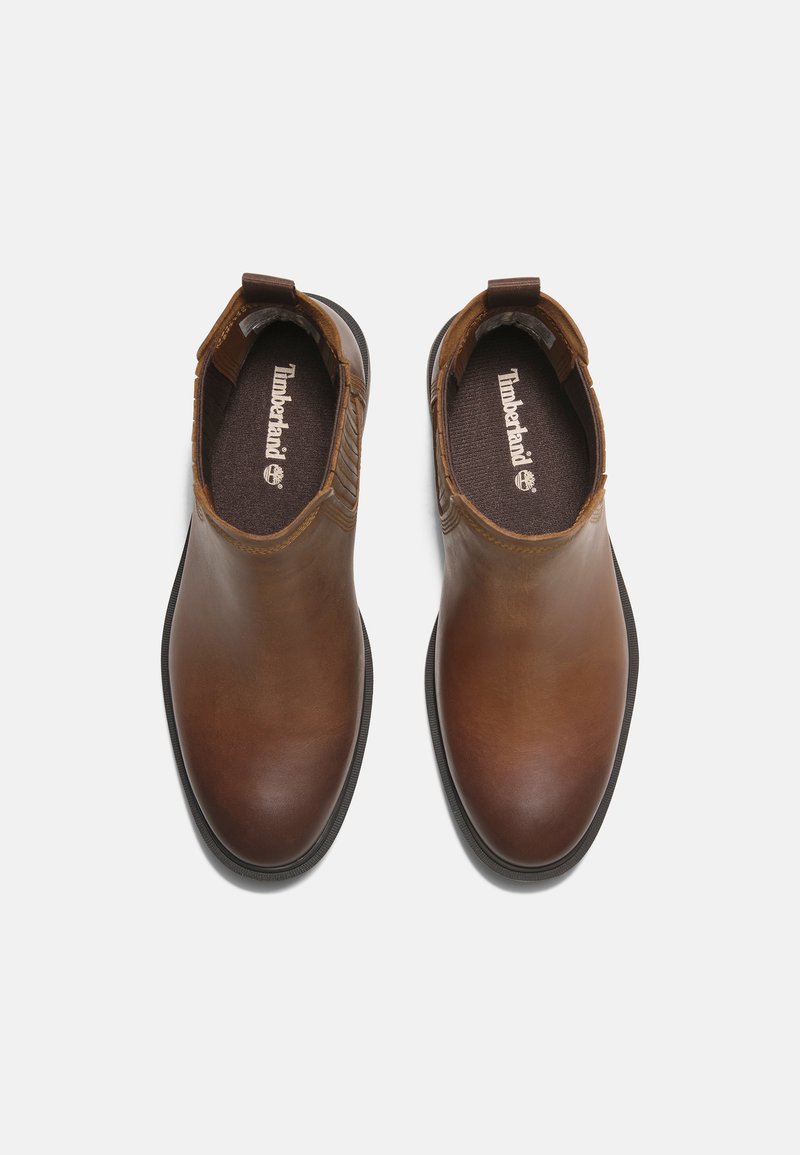 Bruine leren enkellaarsjes met elastische zijkanten, ronde neus en een gestructureerd contrasterend detail aan de zijkanten. Rubber zool.