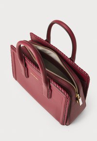 Burgundy läderhandväska med flätade detaljer, dubbla handtag på toppen och en guldfärgad dragkedja. Insidan har en ljus foder.