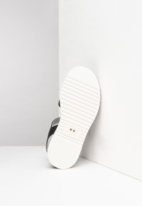 Sandalia negra con una suela de goma blanca de textura acanalada. La plantilla tiene un ligero arco y una etiqueta de marca prominente.