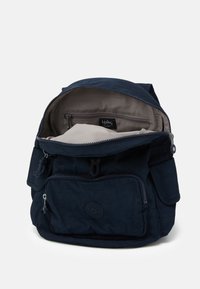 Tummansininen kangaskassi, jossa on vetoketjukiinnitys, ulkopuolisia taskuja ja teksturoitu pinta. Sisäpuolella on vaaleasävyinen vuori.