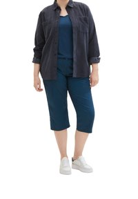 Námorně modrá manšestrová košile na knoflíky přes tmavě modrý tílko, spárovaná s tyrkysovými cropped kalhotami a bílými teniskami. Obsahuje kapsy a manžety.