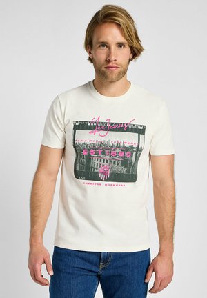 White cotton t-shirt with short sleeves. Front features a graphic design with a cityscape, pink and black accents, and text branding.