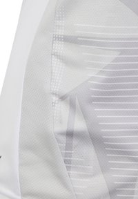 Tessuto atletico bianco con una superficie testurizzata. Presenta motivi geometrici in grigio chiaro e sottili accenti a pois. Visibili i dettagli delle cuciture.