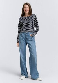 Zwart-wit gestreept shirt met lange mouwen en lichtblauwe jeans met wijde pijpen. De jeans hebben een hoge taille en voorzakken, gecombineerd met witte sneakers.