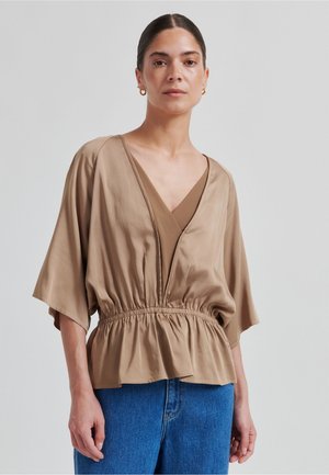 Blusa in raso marrone con scollo a V profondo, vita elastica e maniche ampie, abbinata a pantaloni di jeans blu. Tessuto liscio e vestibilità comoda.