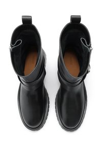 Pár čiernych kožených členkových boots s hrubými podrážkami a popruhmi, pohľad zhora na bielom pozadí.