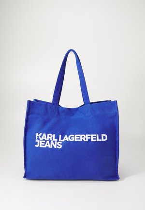 Sac fourre-tout en toile bleu avec deux poignées, affichant un grand texte blanc qui dit "KARL LAGERFELD JEANS" à l'avant. Design simple.