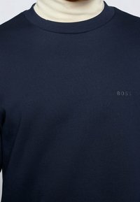 Marinblå crew-neck sweatshirt i mjukt material, med ribbad krage och en subtil präglad "BOSS"-logotyp på bröstet.