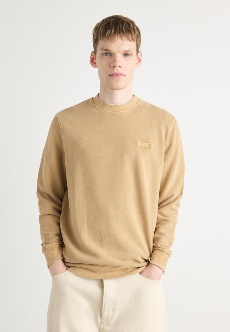 Sweatshirt bege com uma textura suave, apresentando um decote redondo e um logótipo bordado no lado esquerdo do peito. Ajuste relaxado, mangas longas.