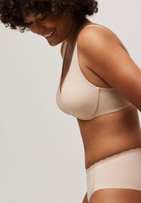 Sostén inalámbrico beige liso y braguitas tipo hipster a juego con bordes ondulados, que cuentan con un diseño sin costuras y una textura de tela suave.