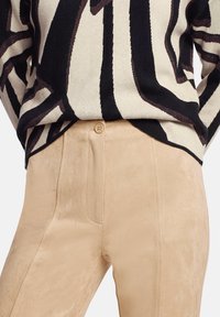 Pull à motif abstrait noir et beige rentré dans un pantalon en daim marron clair taille haute avec fermeture à bouton.
