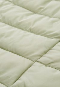 Nahaufnahme von hellbeigem, gestepptem Stoff mit horizontaler Naht und weicher, gepolsterter Textur.