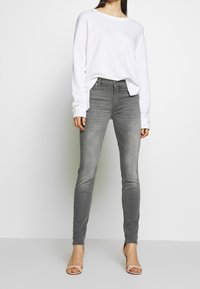 Šedé džíny se slim fit a vybledlým vzhledem, zkombinované s volně střiženým bílým svetrem a béžovými podpatky. Jednoduchý design bez vzorů.