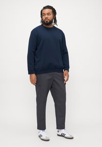 Marineblaues Sweatshirt mit Rundhalsausschnitt und langen Ärmeln, kombiniert mit grauen Cargo-Hosen mit Seitentaschen und weißen Schuhen mit schwarzen Streifen.