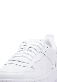 White leather sneaker featuring round toe, flat laces, perforations on the toe box, and logo detail on the tongue and side. Textured sole.
