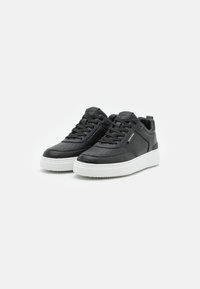 Czarne skórzane sneakersy z perforowanym czubkiem, białą gumową podeszwą, płaskimi czarnymi sznurowadłami oraz szczegółem z logo po bokach. Okrągły czubek i wyściełany kołnierz.