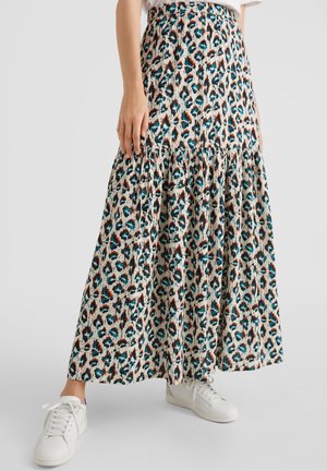 Woman wearing a long, flowy skirt with a blue, brown, and black abstract pattern, paired with white sneakers on a gray background.