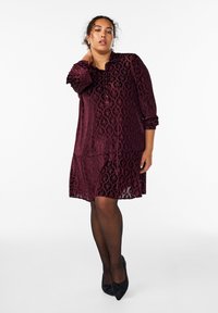 Burgundowa koronkowa sukienka z długimi rękawami, haftowany kwiatowy wzór, do kolan, warstwowy krój, zestawiona z czarnymi szpilkami w szpic.