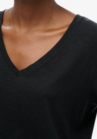 Black V-neck t-shirt made of soft fabric, featuring a small embroidered logo on the chest. Simple design with short sleeves.