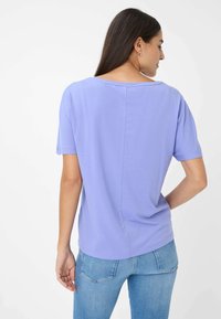 Lilla kortærmet t-shirt med en afslappet pasform, der har en bred halsudskæring og en diskret sømdetalje langs ryggen. Båret med lyseblå jeans.