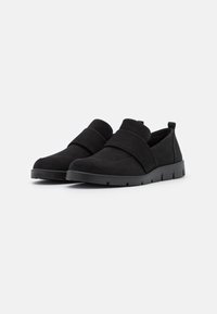 Juodi zomšiniai slip-on batai su apvalia nosimi, elastingomis juostelėmis viršuje ir tekstūruotu guminio pado, turinčio griovelius sukibimui.