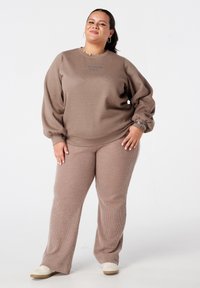 Bruine gebreide sweatshirt met textuur en ballonmouwen, met de tekst "LE WEEKEND". Gecombineerd met bijpassende bruine geribde broek en lichtgekleurde schoenen.