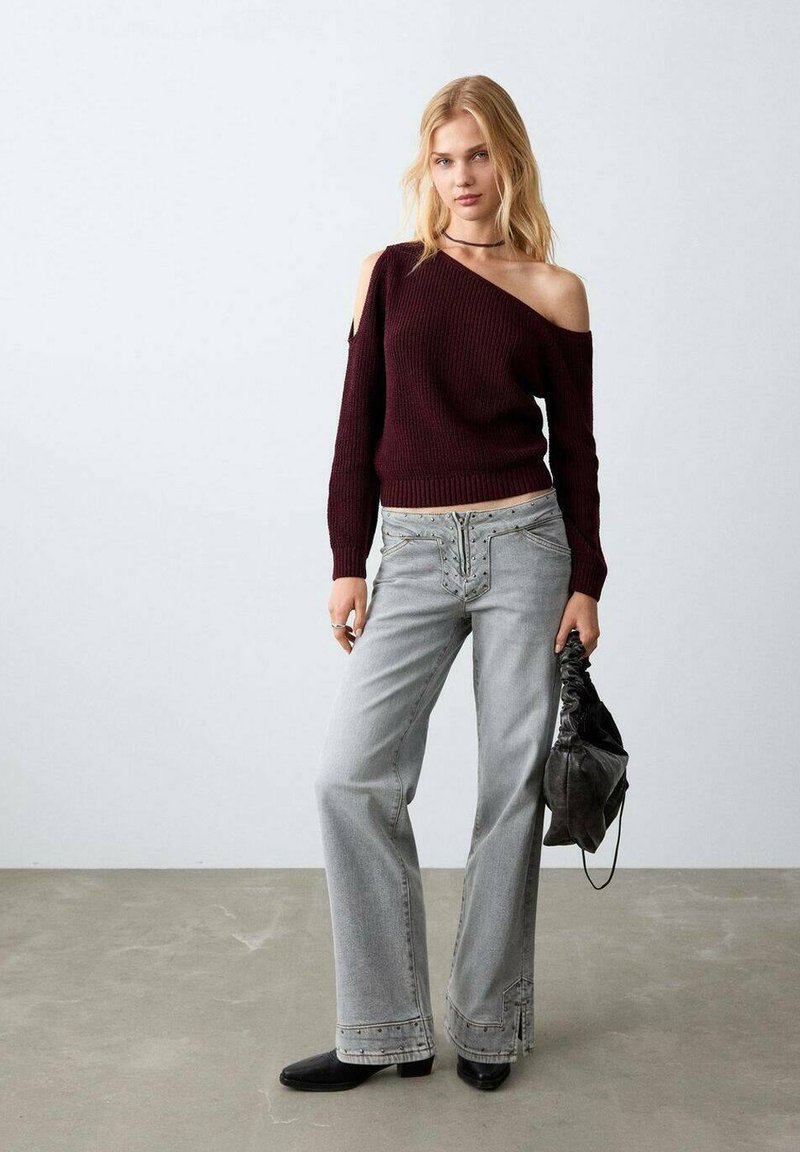 Pull côtelé bordeaux à épaules dénudées, jean gris à jambes larges avec coutures décoratives, sac noir et chaussures noires. Textures lisses, design décontracté.