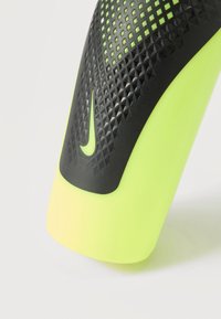 Κοντινή λήψη από φουσκωτό κίτρινο προστατευτικό κνήμης με υφή για καλύτερη πρόσφυση σε μαύρο χρώμα και μικρό λογότυπο Nike στο κέντρο.