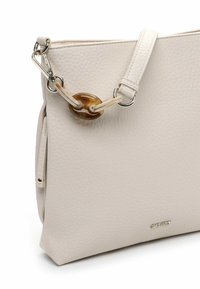 Biała torebka z teksturowanej skóry o gładkim wykończeniu, z unikalnym bursztynowym akcentem metalowym i odpinanym paskiem.