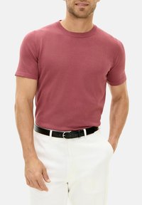 Maglietta a maniche corte, collo rotondo, di colore bordeaux, abbinata a pantaloni bianchi e una cintura nera. Tessuto liscio e design aderente.