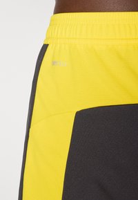 Pantaloni sportivi neri e gialli realizzati in tessuto testurizzato, con una comoda vita elastica e un logo argentato.