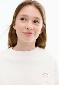 Bílá mikina s texturovanou nášivkou hvězdy a výšivkou "JSTE JEN ÚŽASNÍ" v oranžové barvě, s kulatým výstřihem a uvolněným střihem.