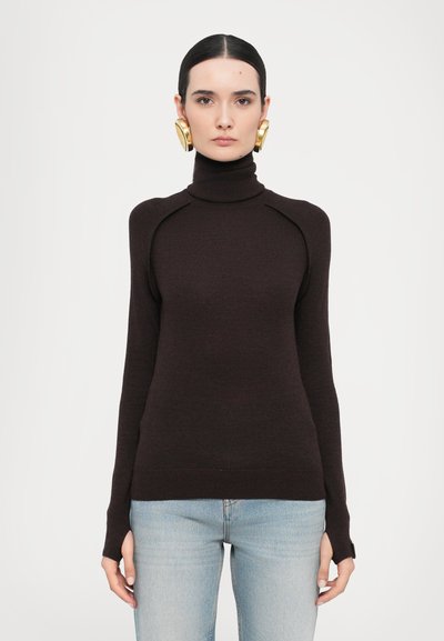 Bruine coltrui met geribbelde textuur, aansluitende silhouet en contrasterende schoudernaden, gecombineerd met lichtblauwe jeans.