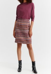 Paita maroon dengan lengan panjang dipadukan dengan rok tekstur berwarna-warni yang memiliki garis horizontal. Sepatu bot pergelangan kaki hitam melengkapi penampilan.