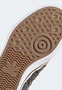 Semelle de sneaker Adidas avec une base en caoutchouc marron texturé, des motifs circulaires et hexagonaux, une semelle intermédiaire blanche, et un détail de logo.